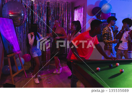 Teenagers enjoying lively dance party with pool table and colorful decorations 135535089