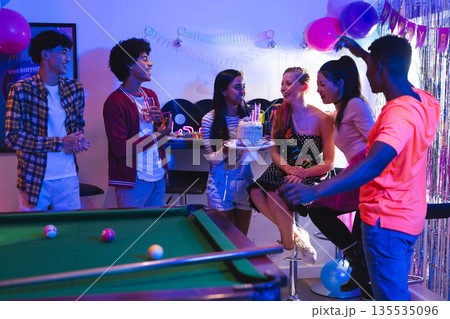 Teens celebrating birthday with cake and decorations in lively party atmosphere Teens celebrating birthday with cake and decorations in lively party atmosphere 135535096