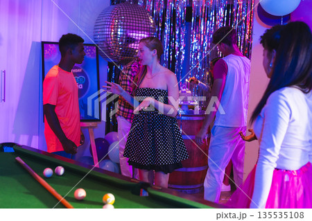 Teenagers enjoying lively party with pool table and disco ball decorations 135535108