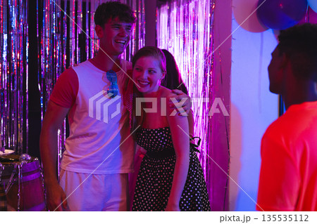 Teens celebrating at party, smiling and enjoying vibrant decorations and lights Teens celebrating at party, smiling and enjoying vibrant decorations and lights 135535112