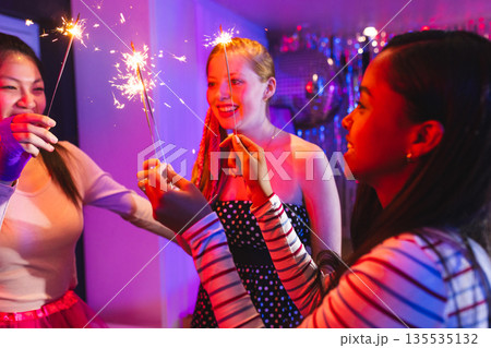 Celebrating at party, teen girls with sparklers, smiling in festive atmosphere Celebrating at party, teen girls with sparklers, smiling in festive atmosphere 135535132