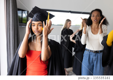 Graduating students in school celebrating academic achievement, adjusting caps joyfully 135535181