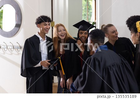 Teen graduates in caps and gowns celebrating together with joyful expressions 135535189