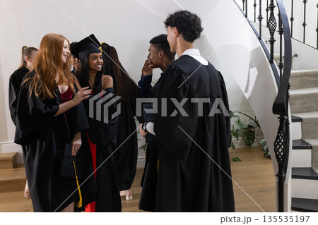 Graduating students in caps and gowns celebrating together at school staircase 135535197
