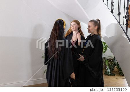 Teen graduates in gowns celebrating and chatting happily at school ceremony Teen graduates in gowns celebrating and chatting happily at school ceremony 135535199