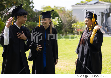 Graduating students in caps and gowns celebrating together outdoors, feeling joyful 135535225
