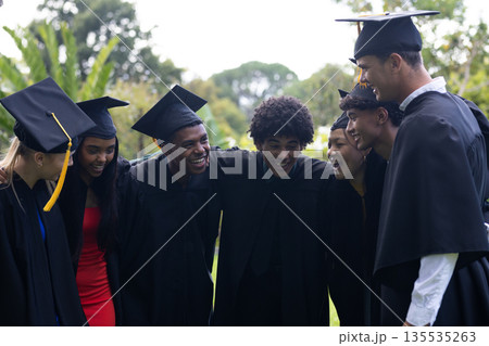 Graduating students in caps and gowns celebrating together outdoors, smiling happily 135535263