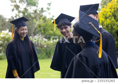 Graduating students in caps and gowns celebrating together outdoors with smiles Graduating students in caps and gowns celebrating together outdoors with smiles 135535265