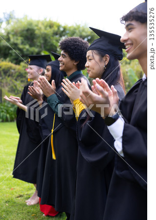 Graduating students in caps and gowns clapping joyfully at outdoor ceremony Graduating students in caps and gowns clapping joyfully at outdoor ceremony 135535276