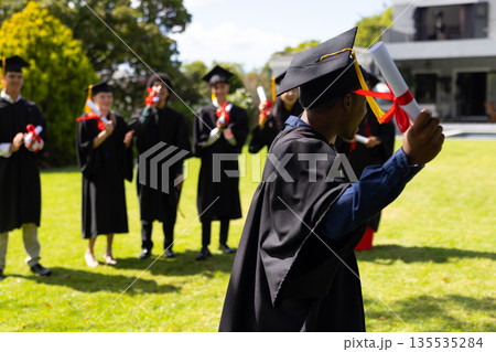 Graduating students celebrating outdoors, wearing caps and gowns, holding diplomas Graduating students celebrating outdoors, wearing caps and gowns, holding diplomas 135535284