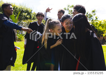 Teen graduates celebrating outdoors, laughing and embracing in graduation gowns Teen graduates celebrating outdoors, laughing and embracing in graduation gowns 135535295