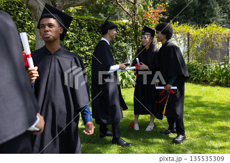 Graduating students in caps and gowns celebrating together outdoors with diplomas Graduating students in caps and gowns celebrating together outdoors with diplomas 135535309
