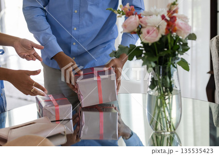 Exchanging gifts, couple wrapping presents at home with flowers on table Exchanging gifts, couple wrapping presents at home with flowers on table 135535423