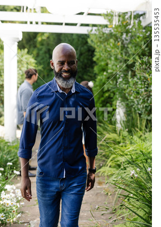 Smiling African American man walking through garden at wedding celebration Smiling African American man walking through garden at wedding celebration 135535453