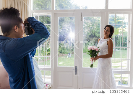 Bride holding bouquet posing for photographer in bright, elegant room Bride holding bouquet posing for photographer in bright, elegant room 135535462