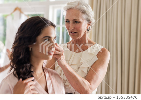 Elderly woman adjusting bride's earrings, preparing for wedding ceremony indoors 135535470