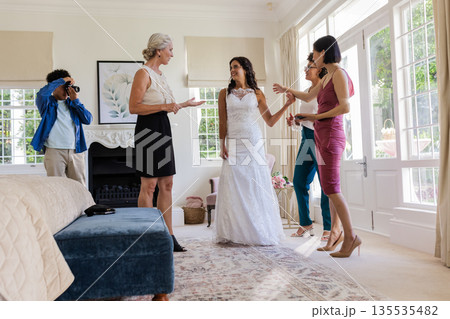 Bride in elegant gown smiling with friends and family in bright living room 135535482