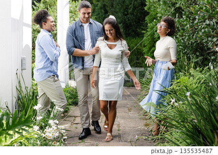 Friends joyfully walking with bride in garden, celebrating wedding day together 135535487