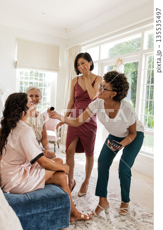 Bridesmaids laughing and applying makeup while getting ready for wedding celebration Bridesmaids laughing and applying makeup while getting ready for wedding celebration 135535497