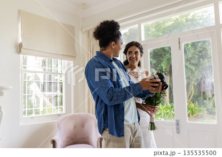 Bride holding bouquet smiling at groom in bright living room, sharing joyful moment Bride holding bouquet smiling at groom in bright living room, sharing joyful moment 135535500