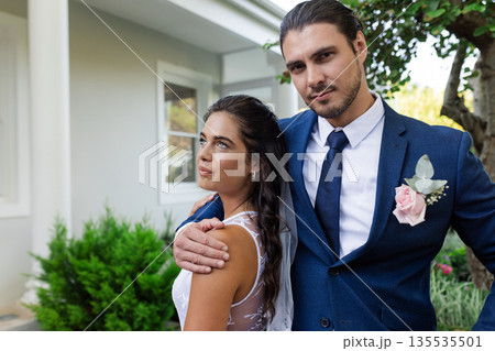 Bride and groom posing together outdoors, embracing and looking content 135535501