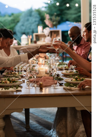 Guests toasting with wine glasses at elegant outdoor wedding dinner table Guests toasting with wine glasses at elegant outdoor wedding dinner table 135535528