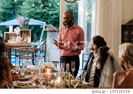 At wedding reception, man giving heartfelt speech, guests listening attentively around table 135535529
