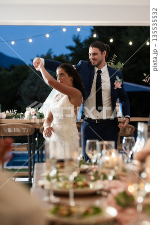 Bride and groom dancing joyfully at outdoor wedding reception under string lights 135535532