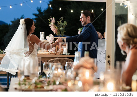 Bride and groom dancing joyfully at outdoor wedding reception under string lights Bride and groom dancing joyfully at outdoor wedding reception under string lights 135535539