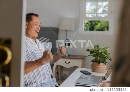 Senior man celebrating success while using laptop at home office desk 135535583