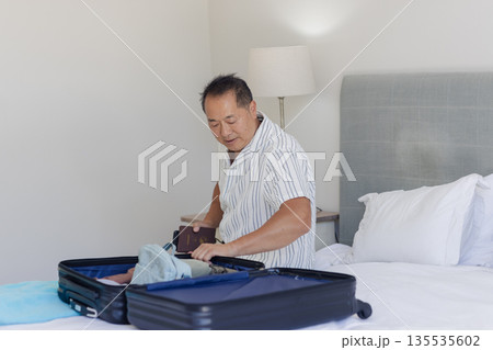 Asian man packing suitcase on bed, preparing for travel with passport Asian man packing suitcase on bed, preparing for travel with passport 135535602