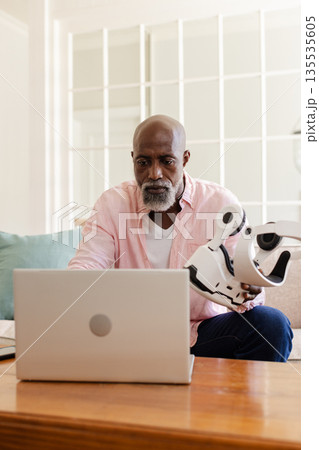 African American man using laptop and holding VR headset at home, concentrating African American man using laptop and holding VR headset at home, concentrating 135535605