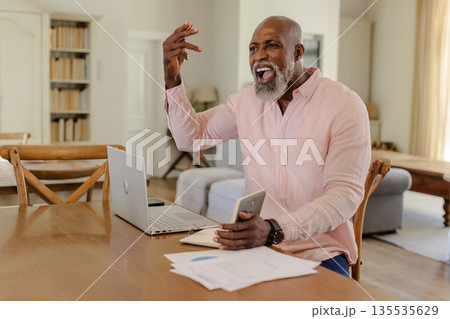 African American man celebrating success at home with laptop and smartphone African American man celebrating success at home with laptop and smartphone 135535629