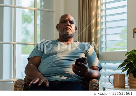 Senior man relaxing at home, holding remote control, enjoying quiet evening 135535661