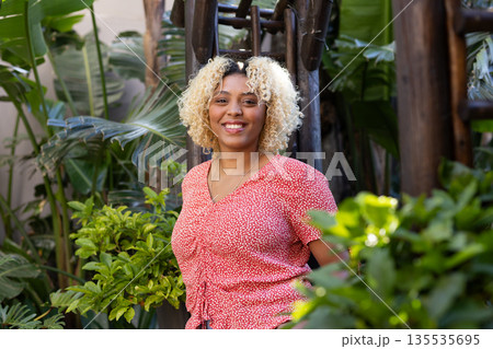 Smiling woman in red blouse enjoying nature surrounded by lush green plants 135535695