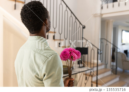 Man holding pink flowers, standing in elegant home, preparing surprise gesture Man holding pink flowers, standing in elegant home, preparing surprise gesture 135535716
