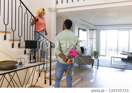 Man surprising woman with flowers at home, standing on staircase, smiling warmly 135535723