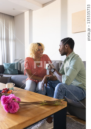 African American friends enjoying coffee and conversation on cozy living room sofa 135535733