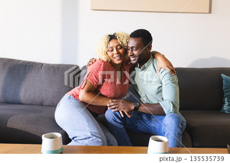 Couple sitting on sofa, embracing and smiling, enjoying quality time together 135535739