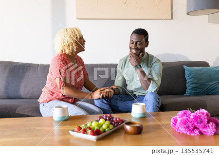 Friends enjoying conversation on sofa, sharing laughter over coffee and snacks Friends enjoying conversation on sofa, sharing laughter over coffee and snacks 135535741