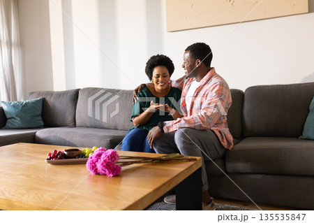 African American couple sitting on sofa, sharing joyful moment at home 135535847