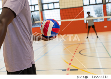 African american male teammates practicing in shorts on court holding ball next to net, copy space African american male teammates practicing in shorts on court holding ball next to net, copy space 135536118