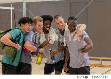 Diverse male friends posing for selfie on volleyball court with smartphone, volleyball 135536119