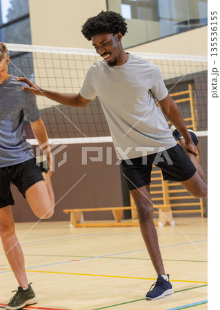 Two male athletes stretching quadriceps on court by volleyball net bench, wall bars, copy space 135536155