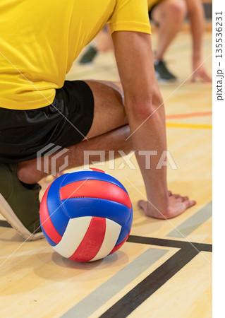Male volleyball partners kneeling on court handling red white blue volleyball and court lines Male volleyball partners kneeling on court handling red white blue volleyball and court lines 135536231