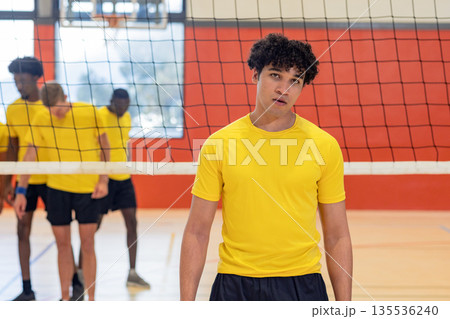 Diverse male volleyball partners in yellow shirts practicing strategy behind net on polished court 135536240