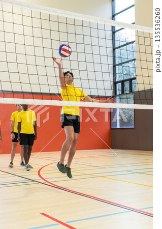 Diverse male teammates jumping, reaching volleyball over net in yellow jerseys on court Diverse male teammates jumping, reaching volleyball over net in yellow jerseys on court 135536260