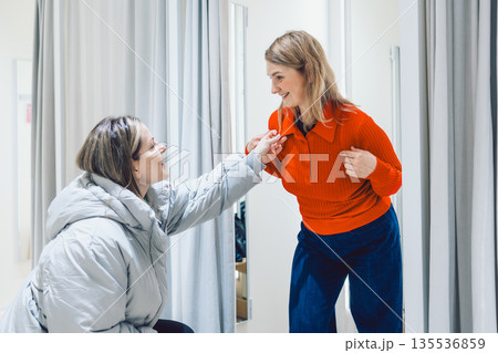 Two women shopping in store trying on clothes in fitting room Two women shopping in store trying on clothes in fitting room 135536859