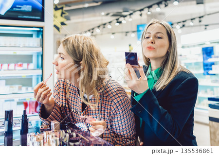 Two cheerful friends are choosing mascara and lipstick in cosmetics store 135536861