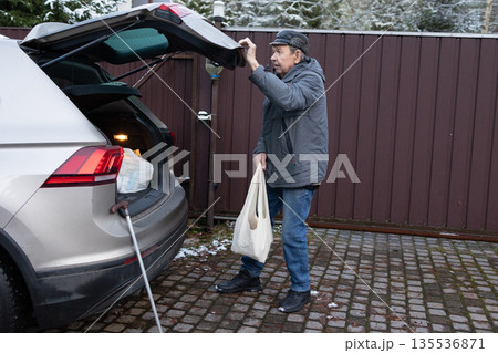 Elderly Man Loading Groceries Into Car Trunk In Winter 135536871
